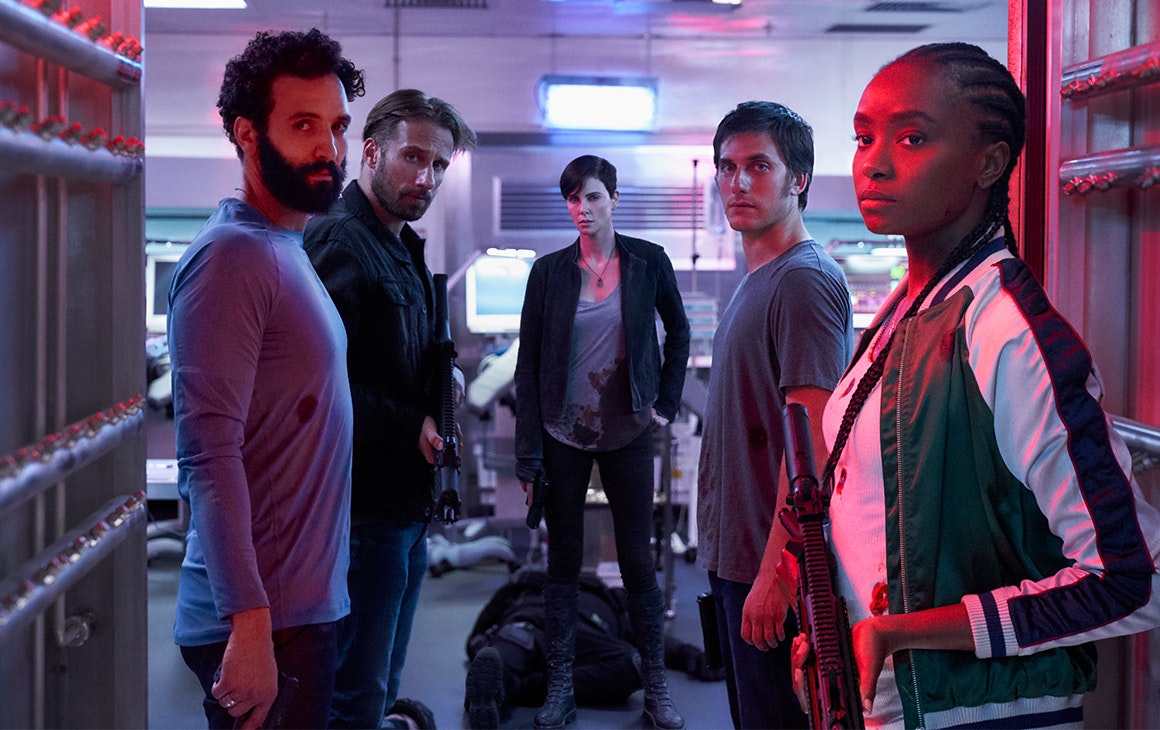 a group of men and women, armed with weapons, stare down the camera